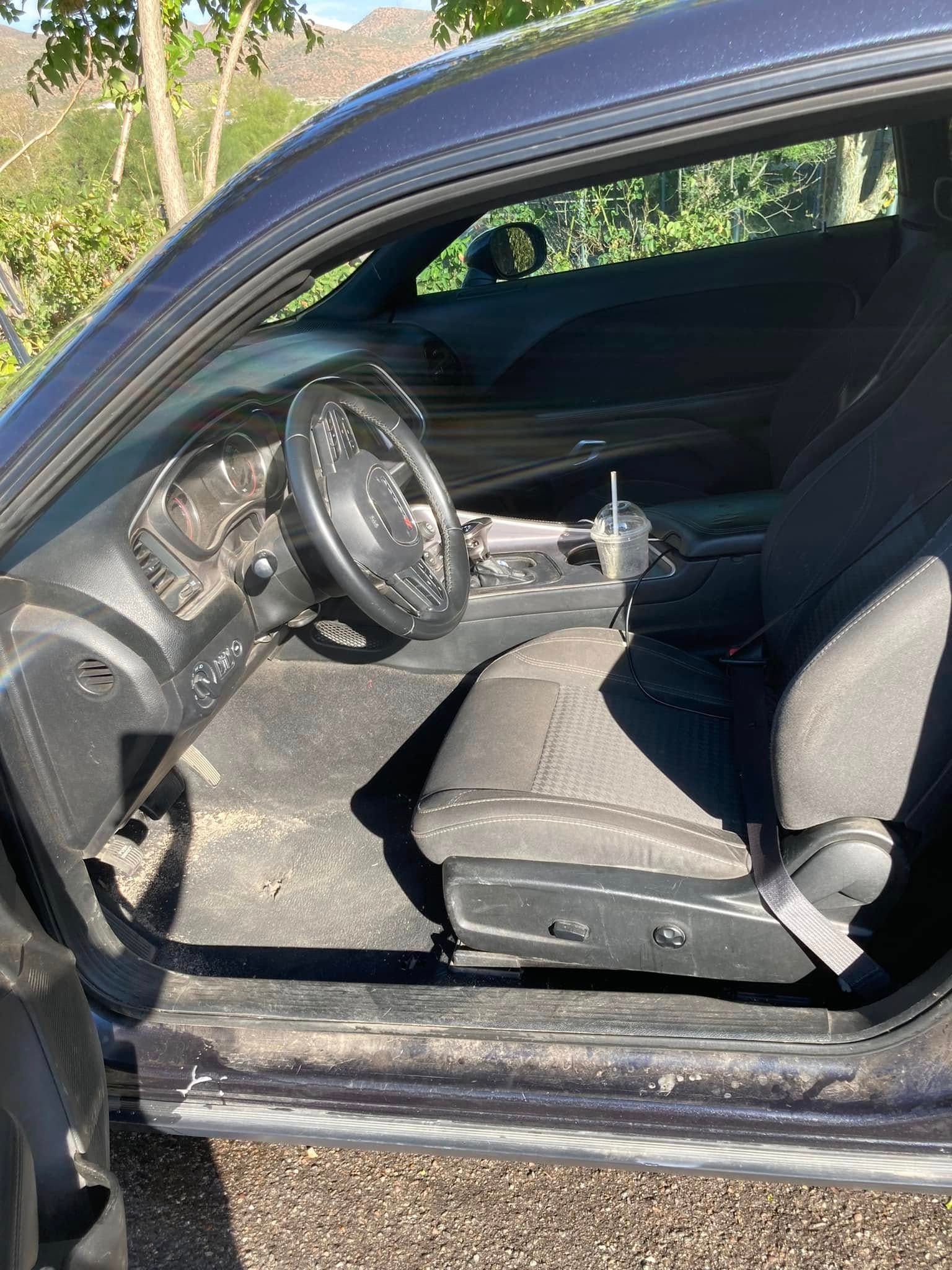Open car door showing a black steering wheel and gray driver’s seat in a sunlit vehicle interior