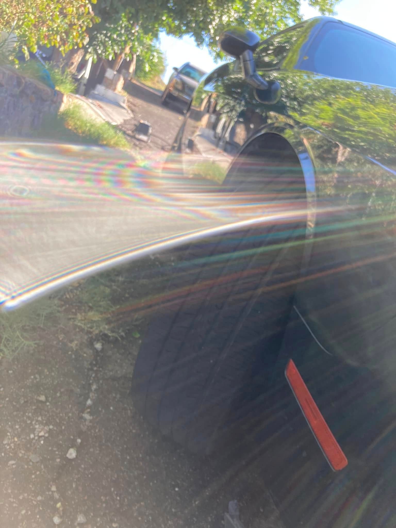 Glare on a car window reflects a bicycle, hedge, and sidewalk in bright sunlight