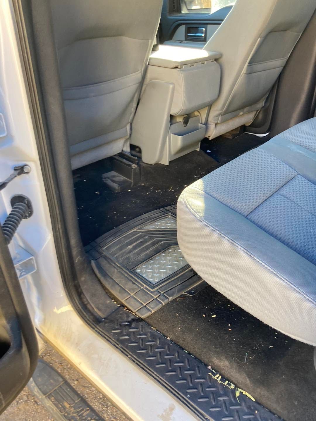 Car interior with front seat backs, black floor mat, and a doorway visible.