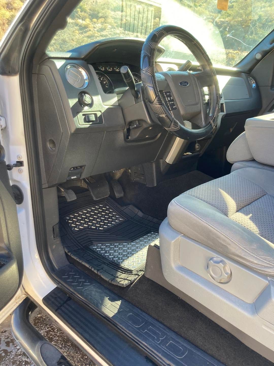 Open truck driver’s seat with black steering wheel, gray interior, and step rail visible