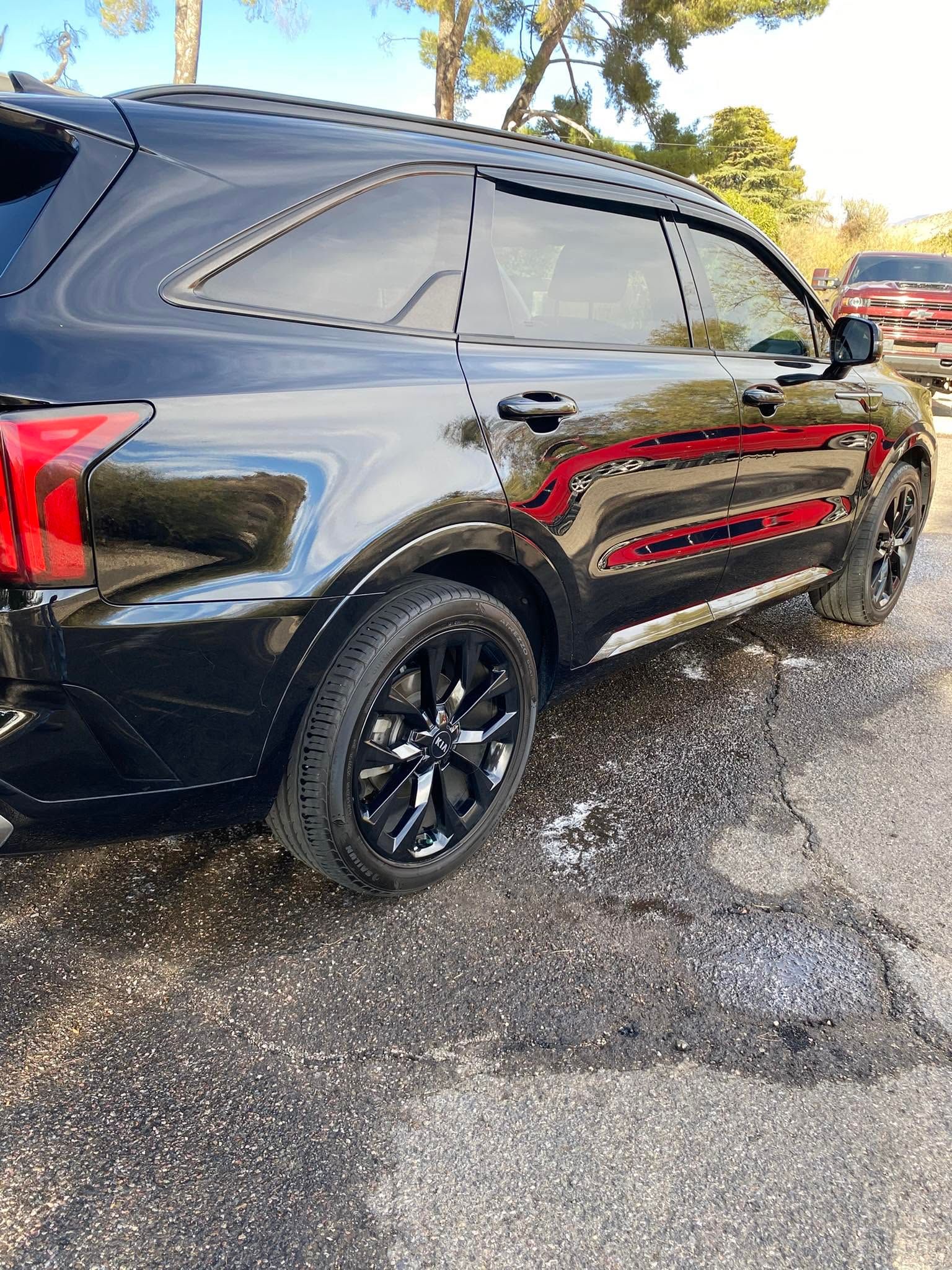 Black SUV parked on wet gravel, side view with tinted windows and red trim.