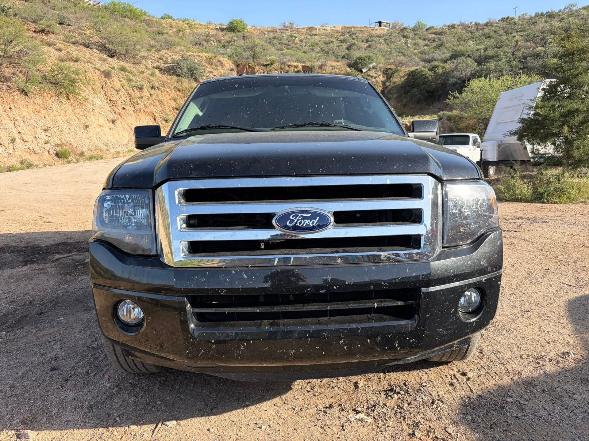 Front view of a black Ford SUV parked on a dirt road in a desert-like landscape.