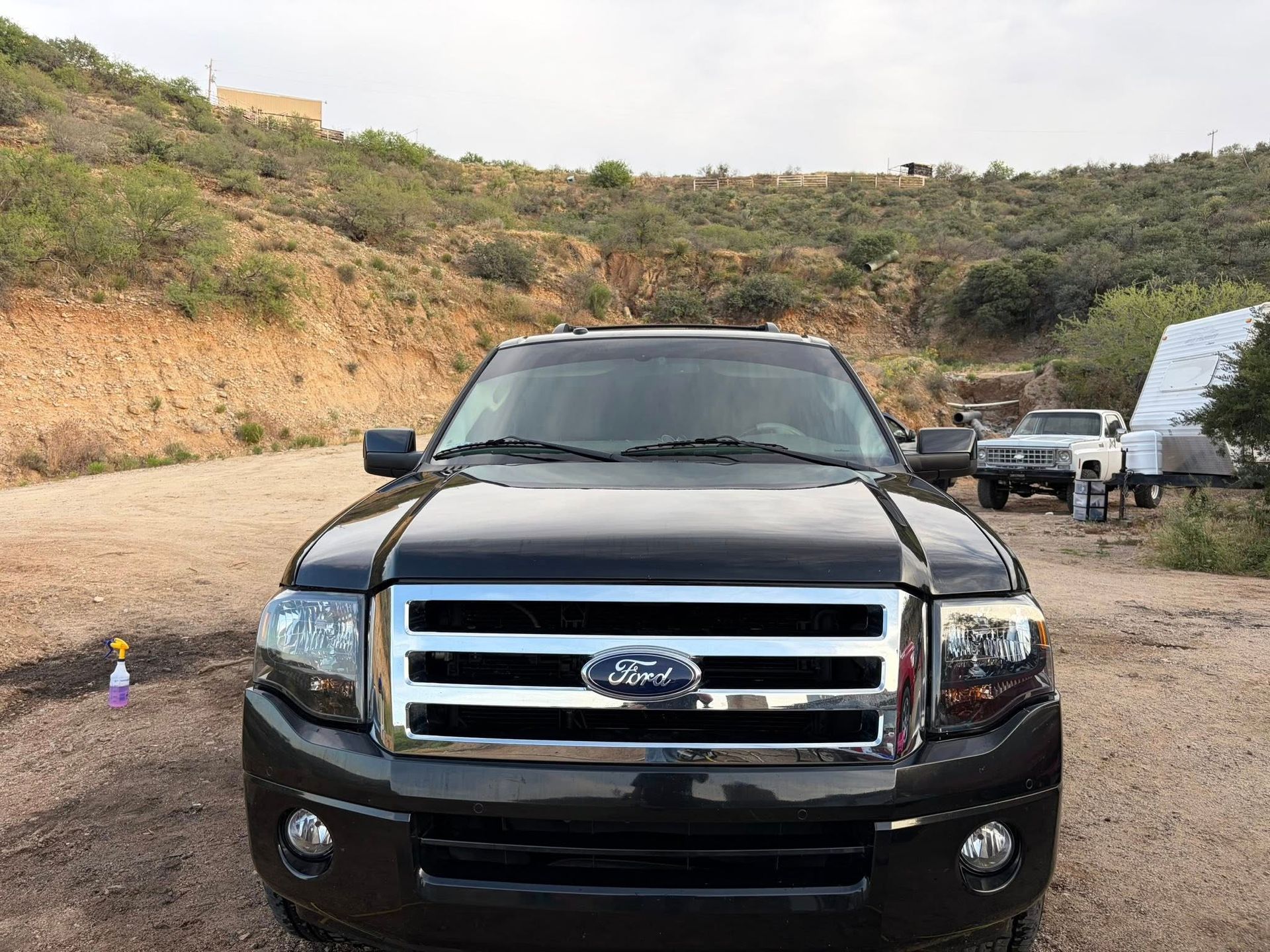 Black Ford SUV parked on a dirt road in a hilly landscape with another vehicle nearby