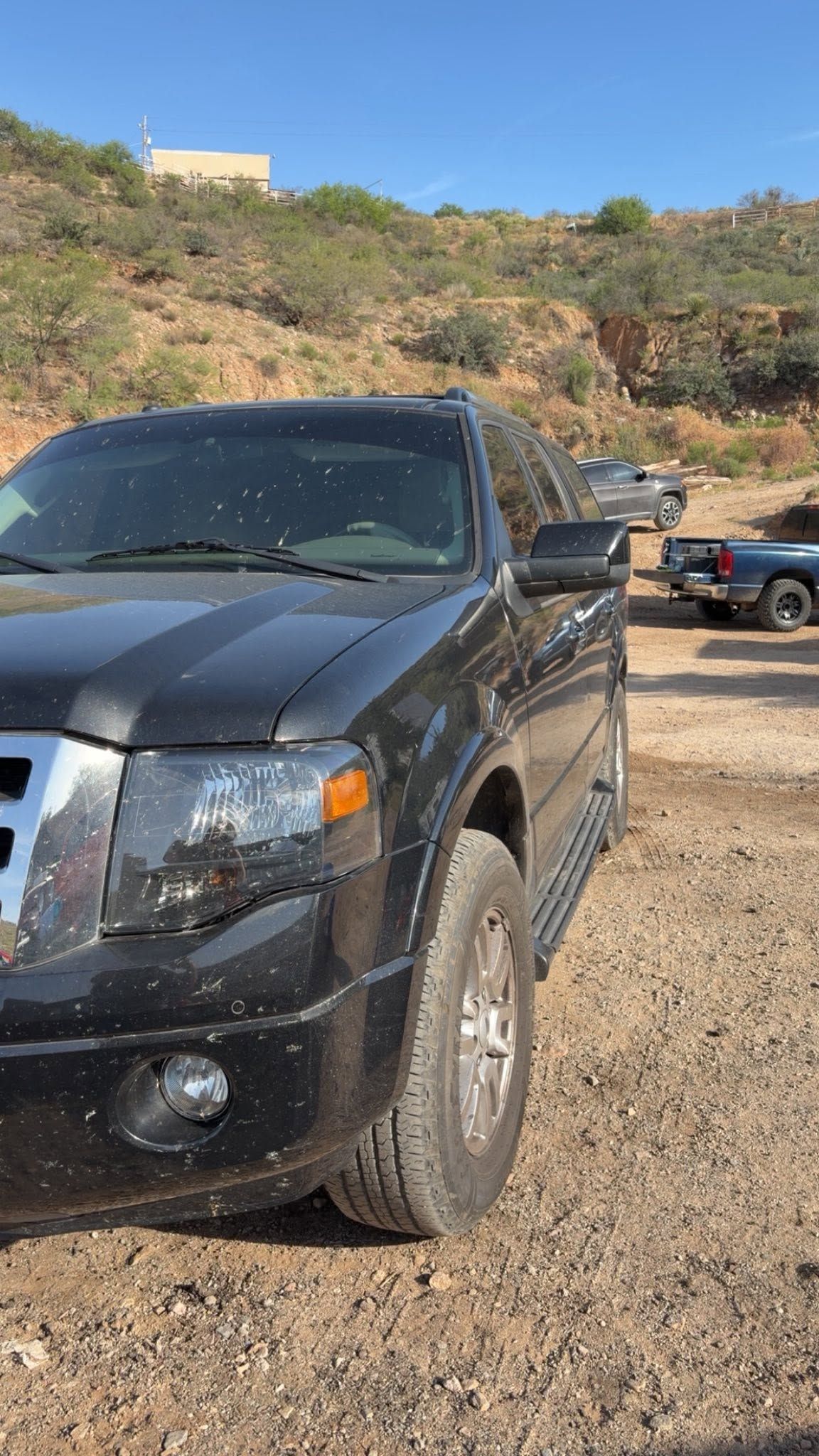 Black SUV parked on a gravel lot with hills and blue sky in the background