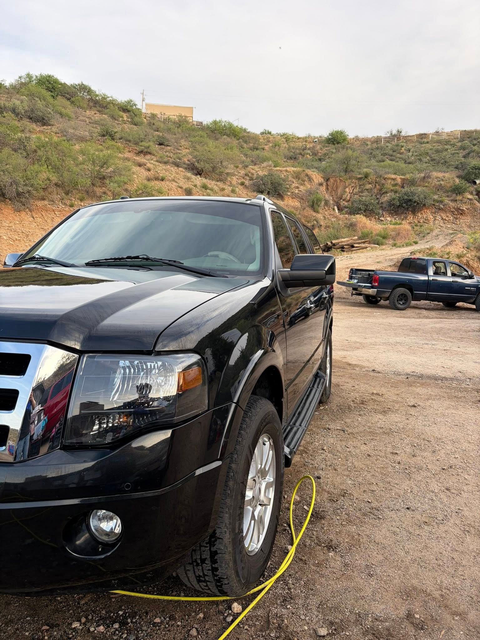 Black pickup truck parked on a dirt road with hills in the background