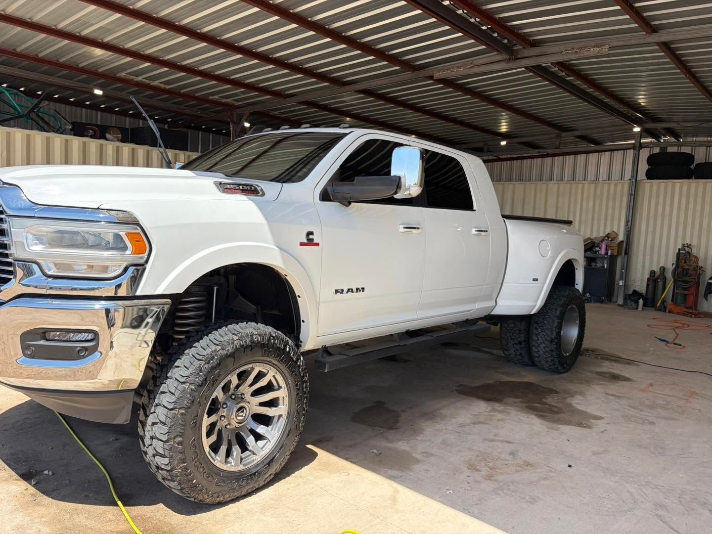 White lifted pickup truck parked in a covered garage with a concrete floor and metal roof.