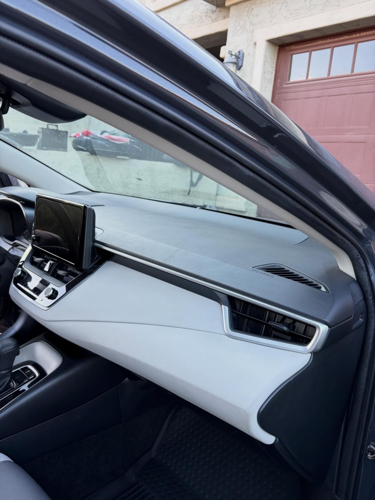 Car interior with dashboard and open passenger door, showing gray and black trim.