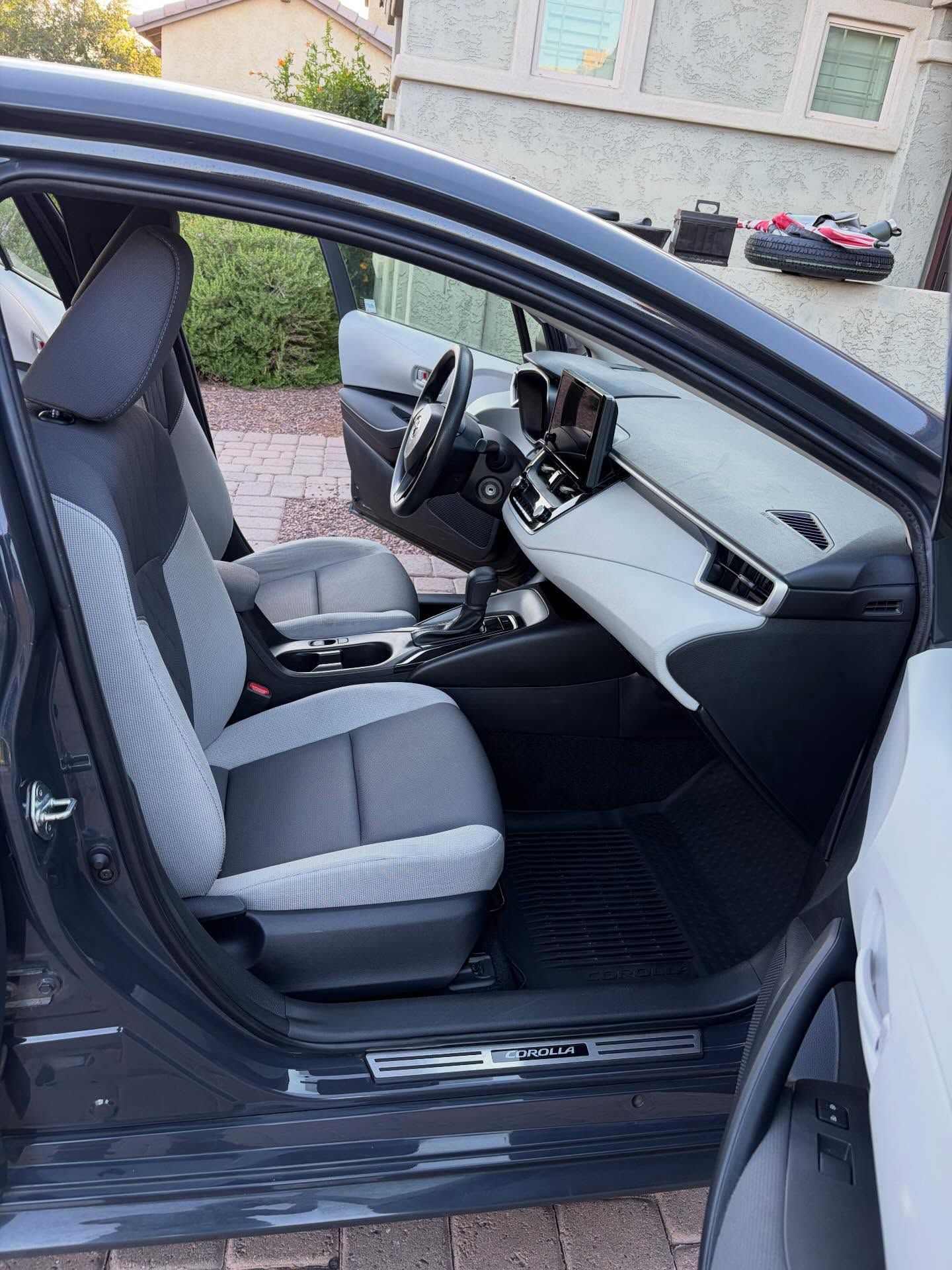 Open car door showing gray front seats and dashboard interior in a driveway