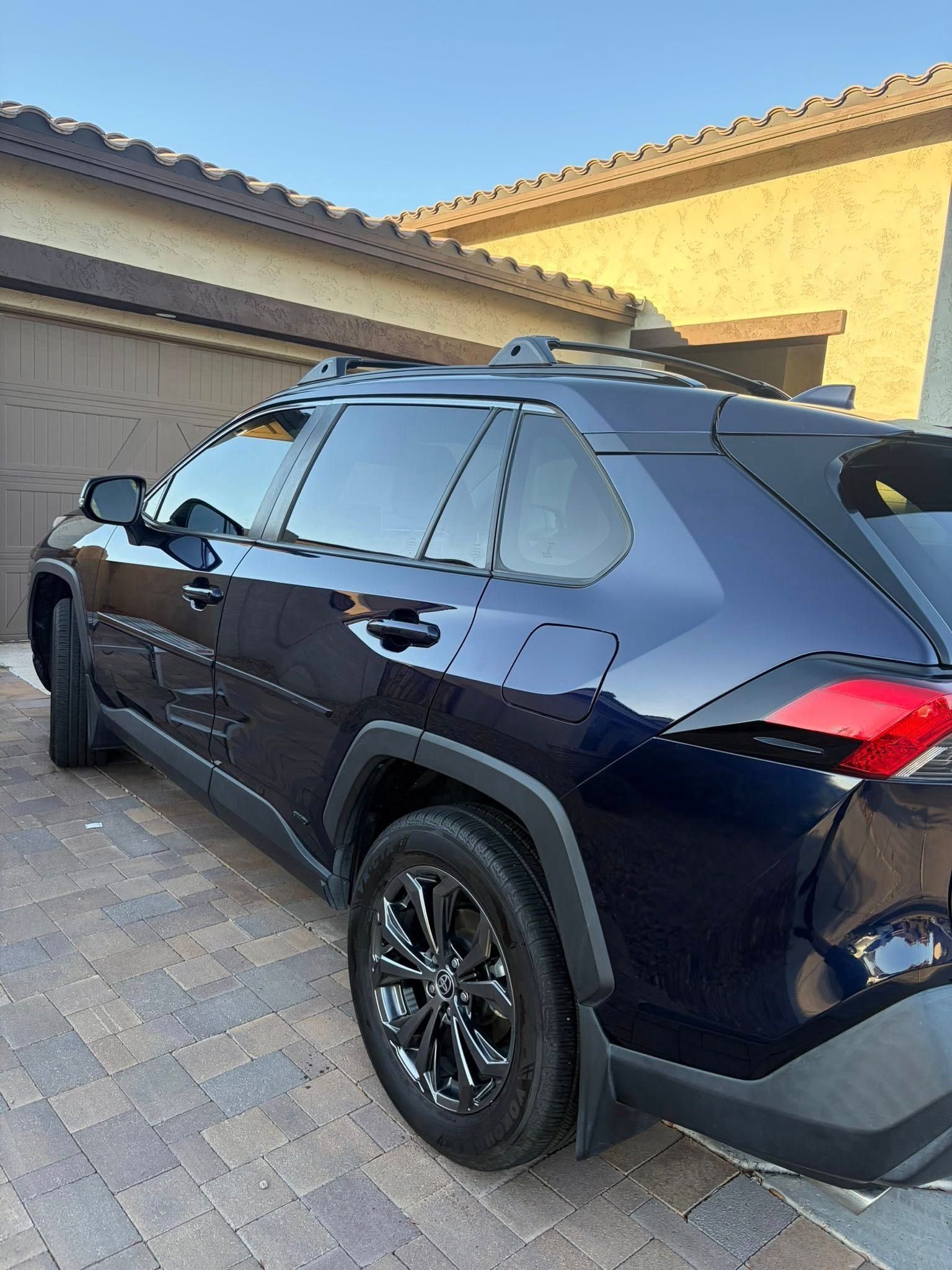 Dark blue SUV parked in a driveway beside a stucco house, viewed from the rear side.