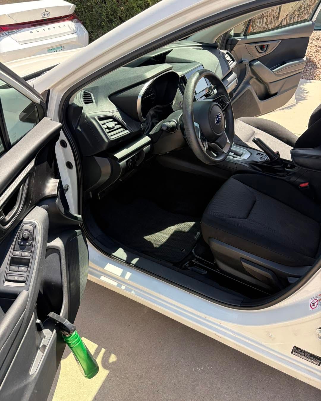 Open car door showing black interior and steering wheel, with a green strap hanging by the door.