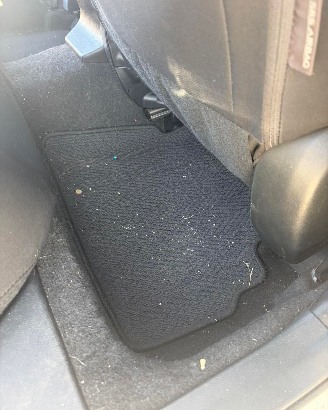 Car floor with black textured mat and the back of a seat