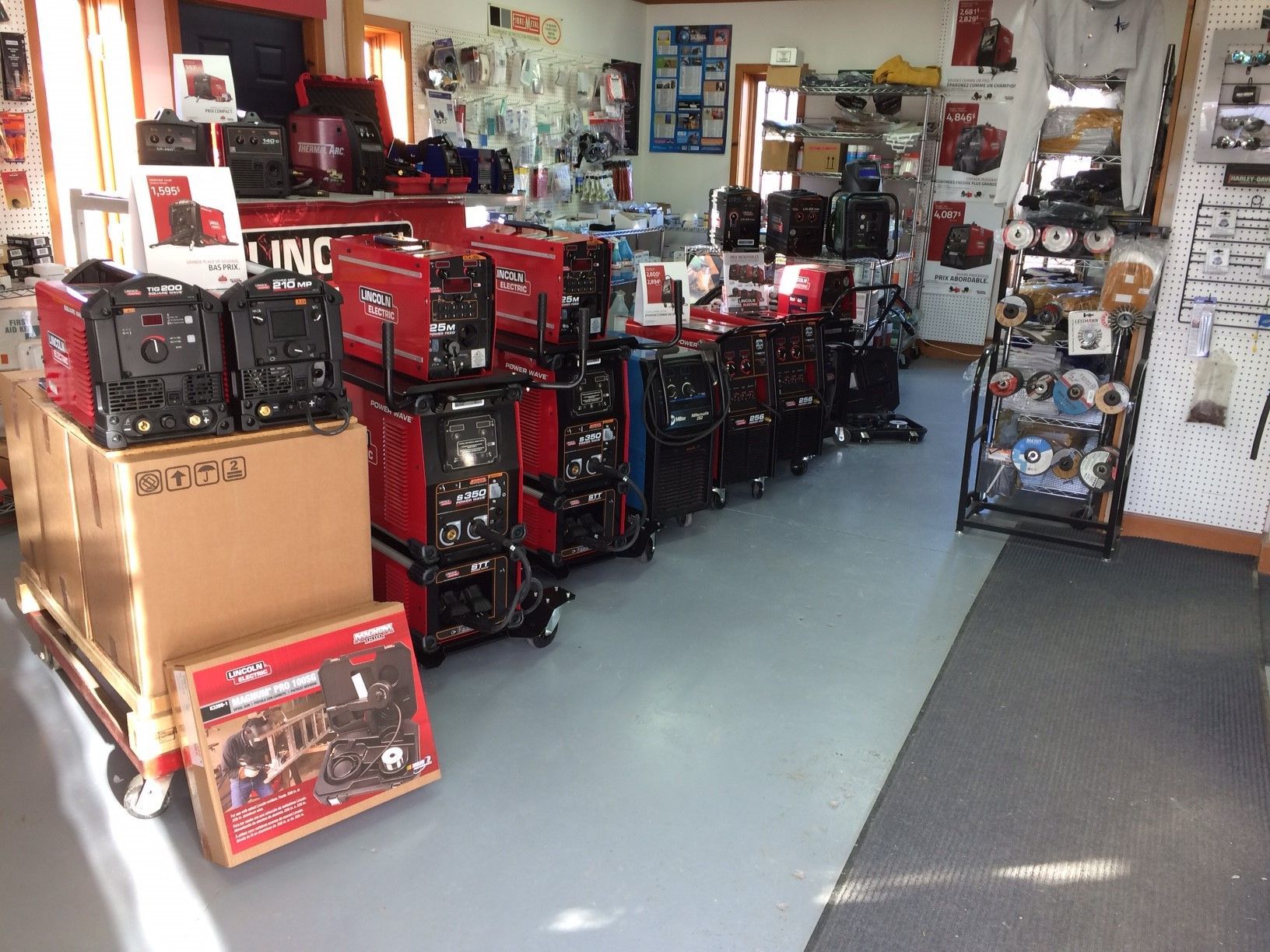 À l'intérieur d'un magasin, plusieurs machines à souder sont exposées, avec des boîtes et d'autres équipements.