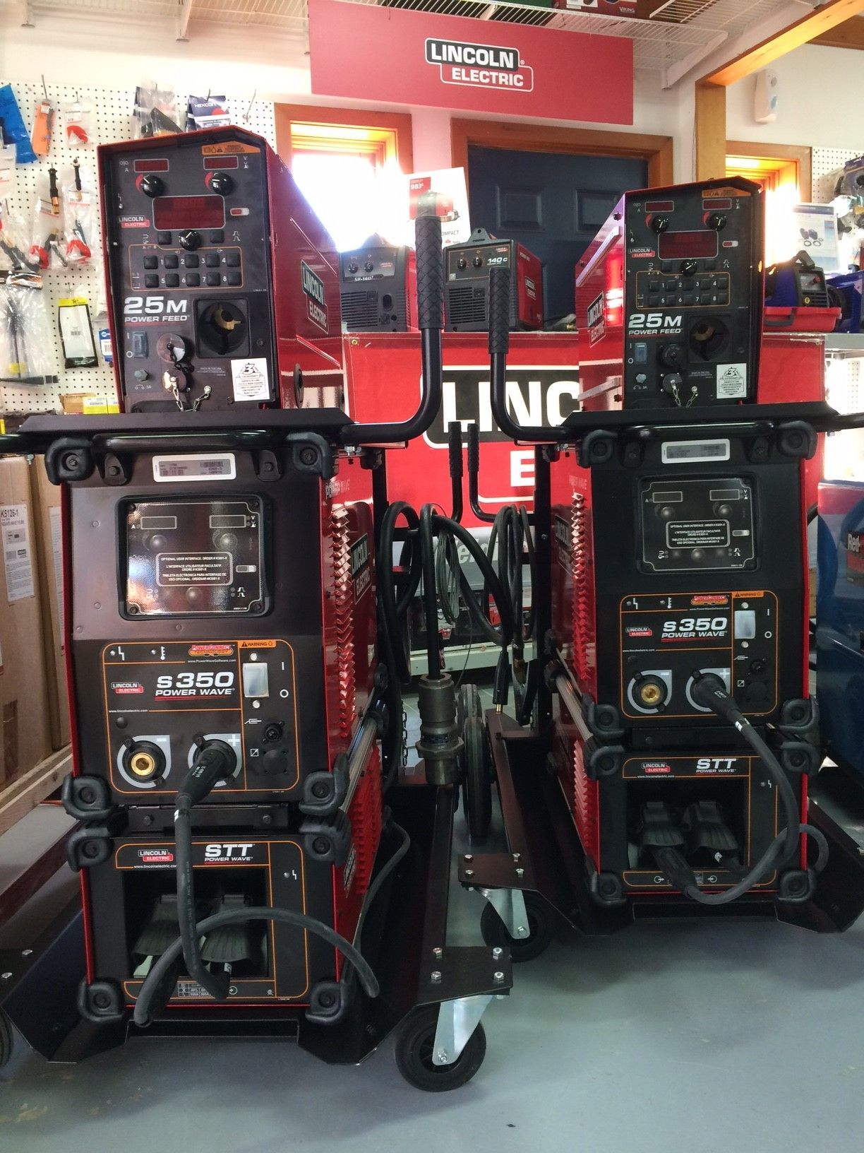 Deux machines à souder Lincoln Electric, une rouge et une noire, sur des chariots à roulettes, dans un magasin.