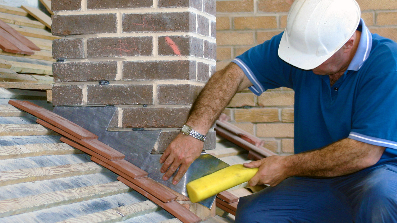 Roofer installing flashing around a brick chimney on a tiled roof.