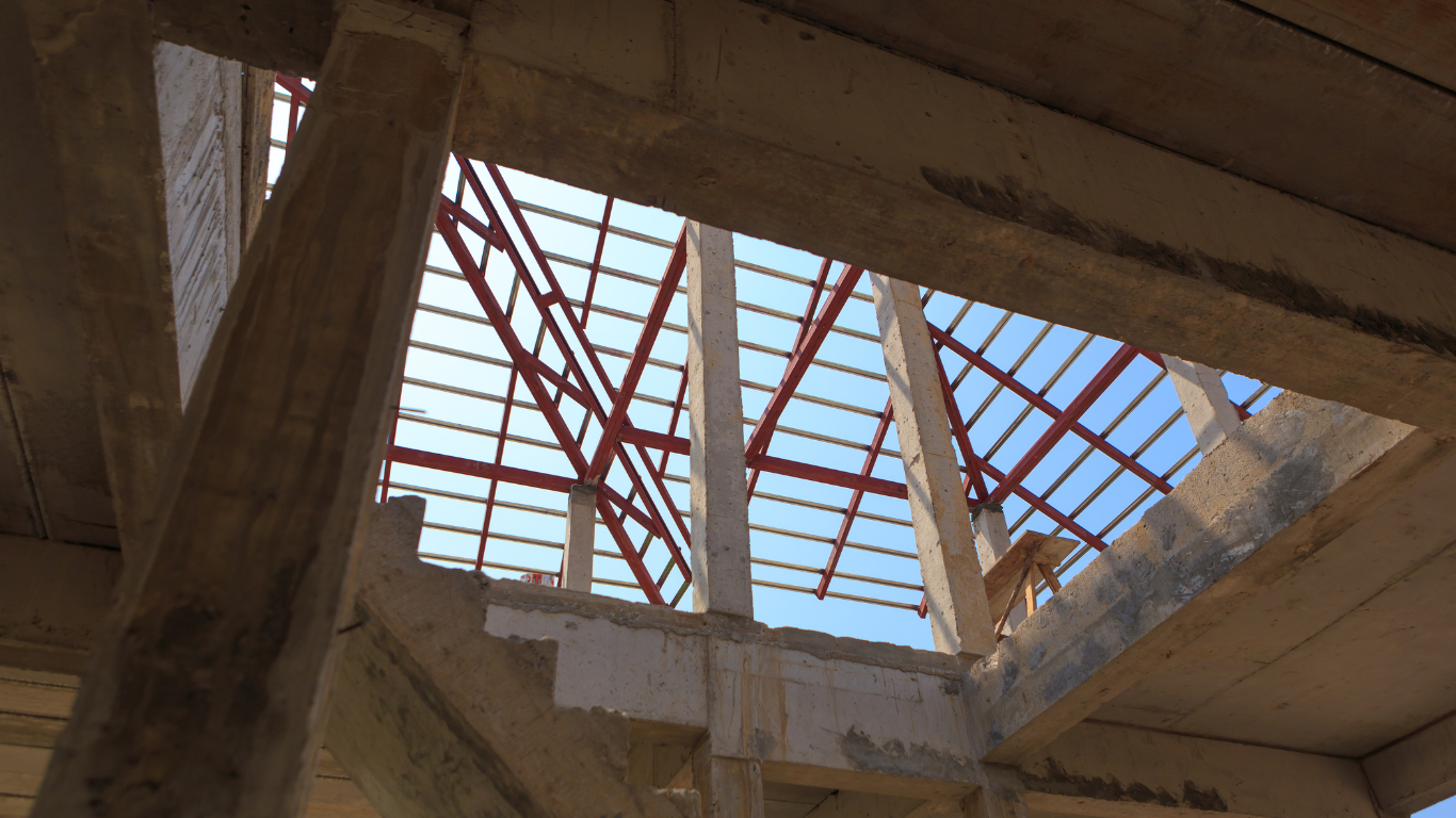 Unfinished building interior with open roof frame visible against a blue sky.