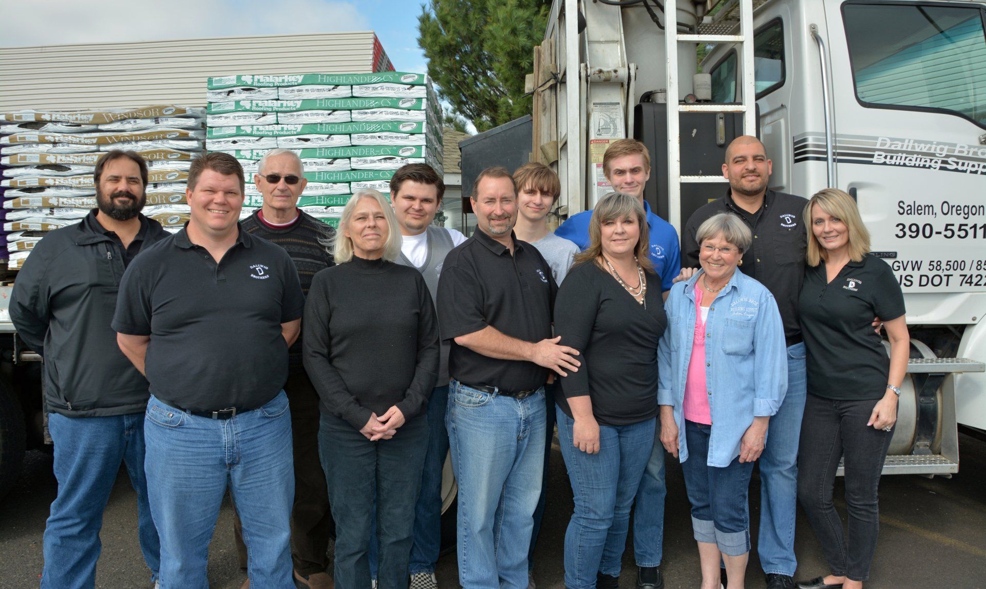 Group of 12 people in front of a truck, some wearing black shirts and jeans.