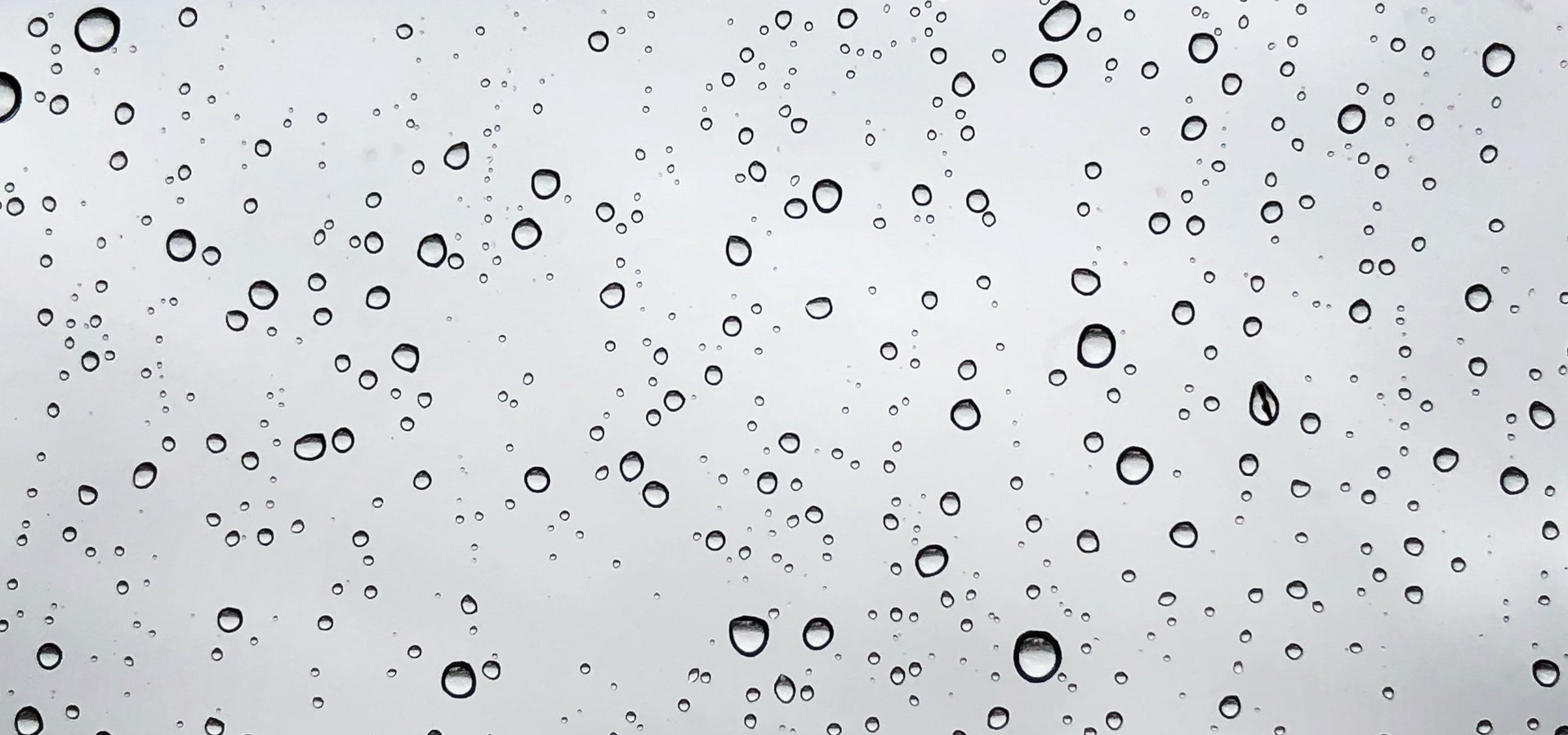 Raindrops on a clear window, against a gray overcast sky.