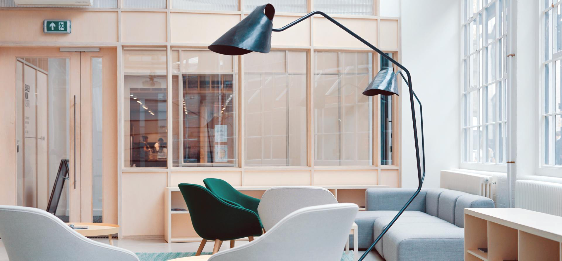 Modern office lounge with teal chairs, gray sofa, and black lamp.