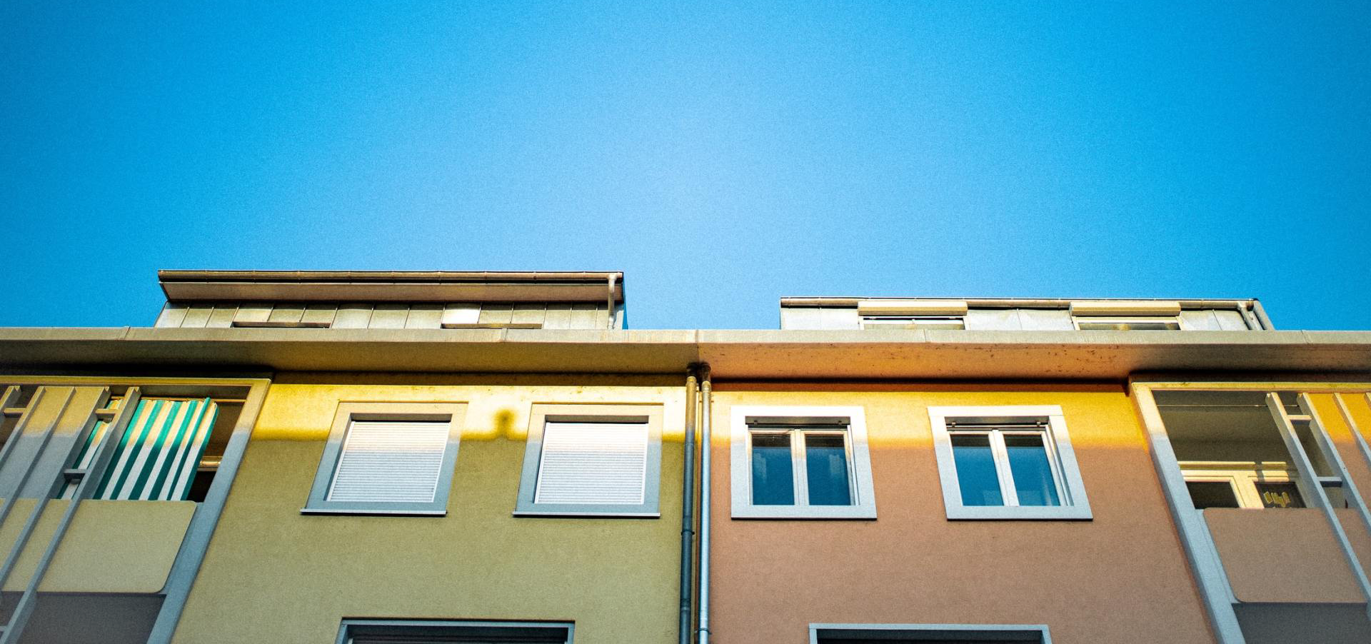 Two-story buildings against a clear blue sky. The buildings are painted yellow and peach.