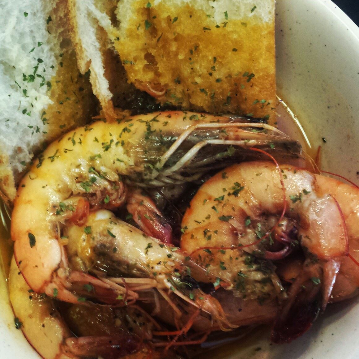 A bowl of shrimp with garlic bread on top