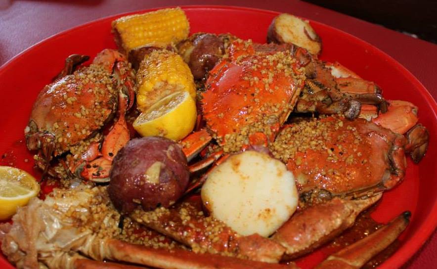 A red plate topped with crabs , potatoes , corn and lemons.