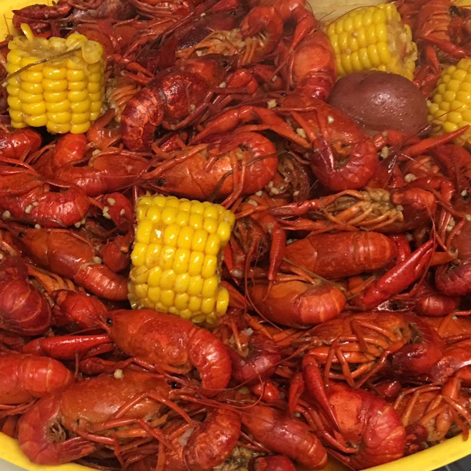 A bowl of crawfish with corn on the cob and potatoes.