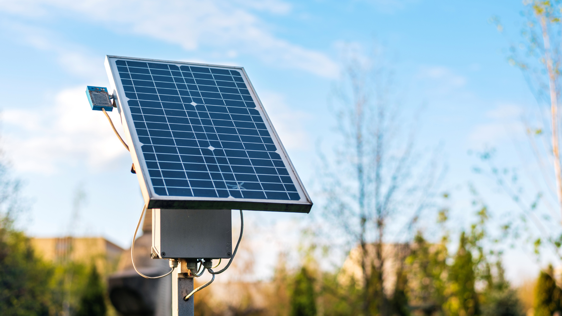 Solar panel on a pole, tilted towards the sun, in a yard, with a blue sky background.