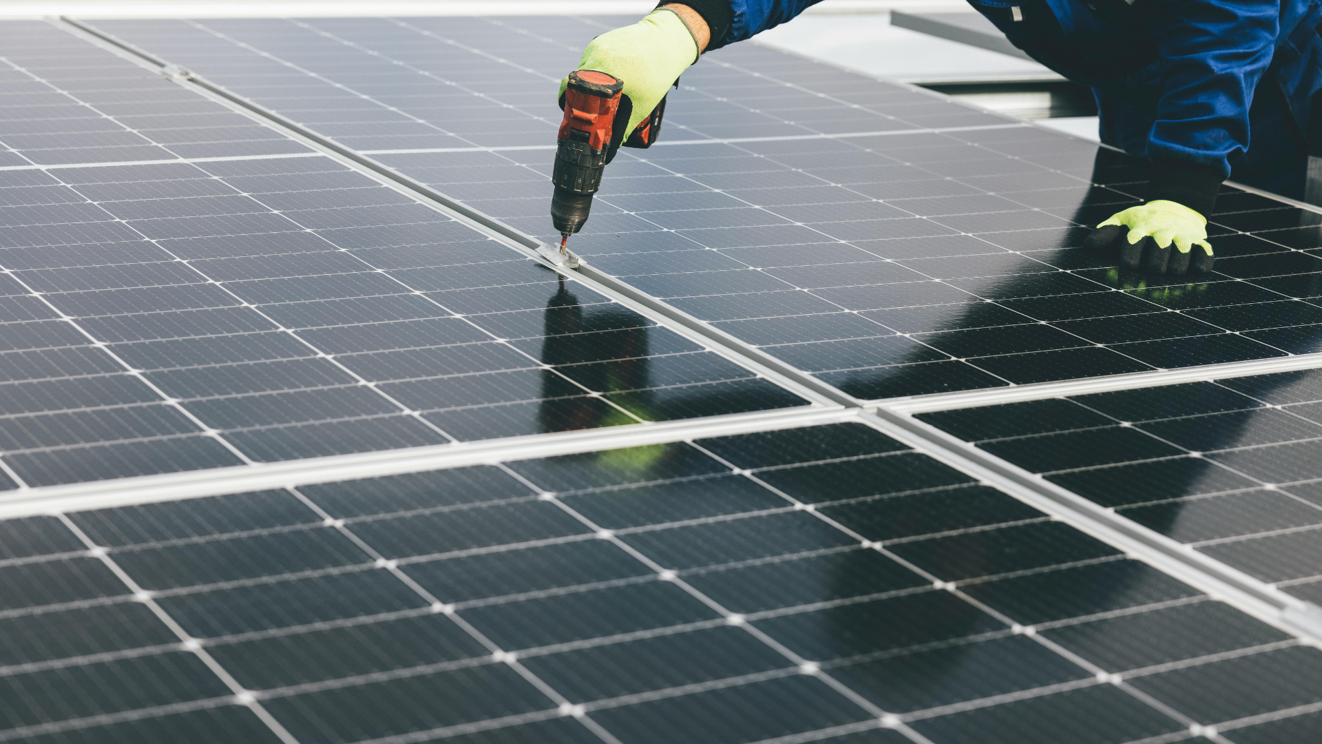 Person wearing gloves installing solar panels with a drill.
