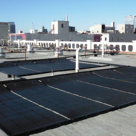 Solar panels on a city rooftop absorb sunlight. Buildings are in the background under a blue sky.