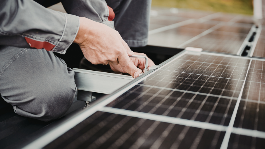 Person installing solar panels on a roof, connecting wiring.