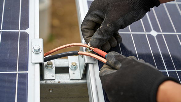 Hands in black gloves connecting wires to a solar panel.