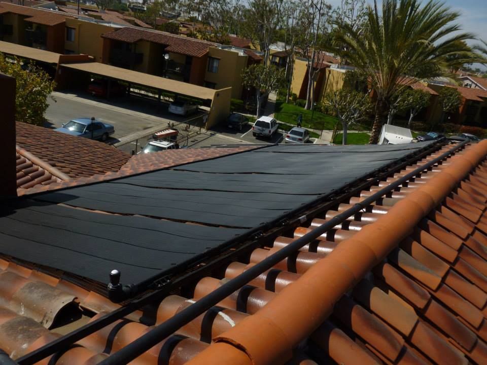 Black solar panels installed on a red tile roof, with apartment buildings and cars in the background.