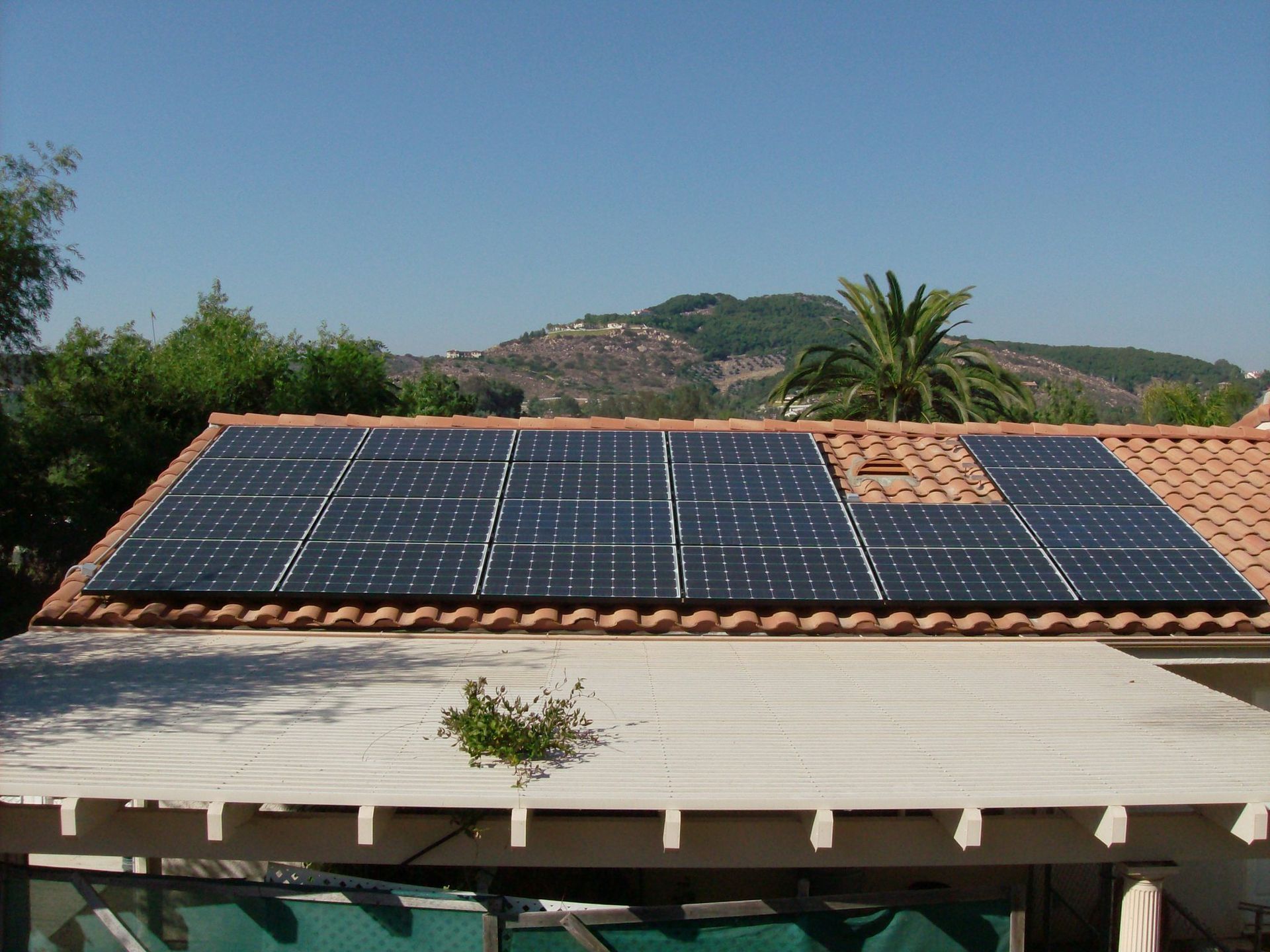 Solar panels on a terracotta tile roof, set against a backdrop of mountains and a blue sky.