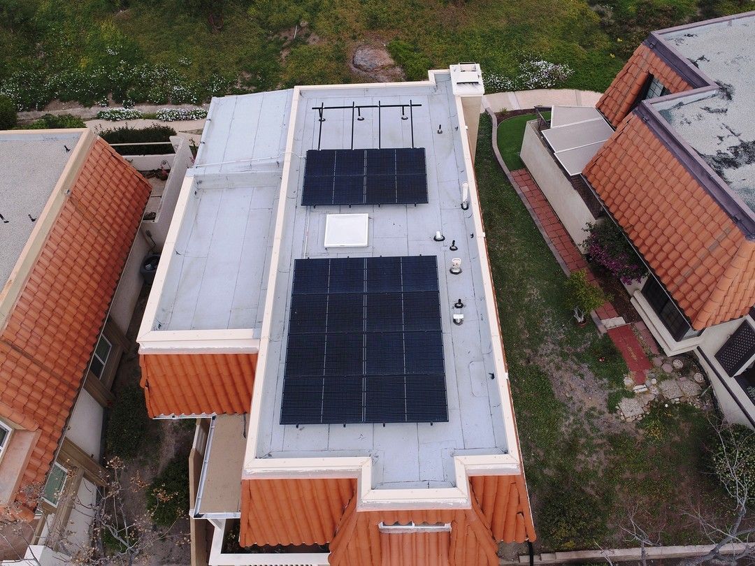 Overhead view of a house roof with solar panels installed on a flat, white portion of the roof.