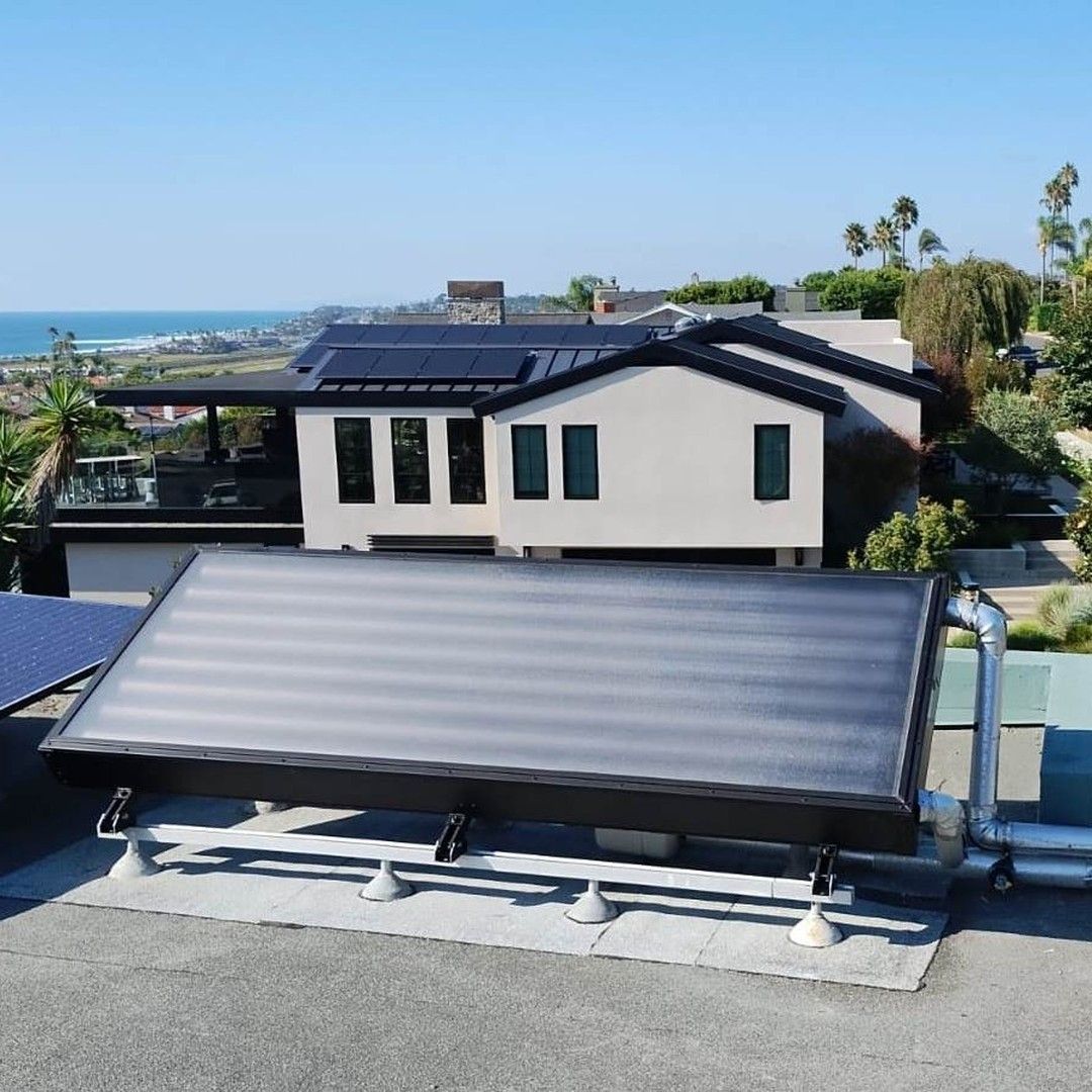 Solar thermal panels on rooftop with house and ocean view in background.