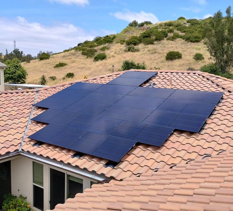 Solar panels installed on a Spanish tile roof against a hillside.
