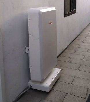 White rectangular solar battery system on a concrete base, mounted on a wall.