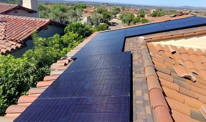 Solar panels installed on a red-tiled roof, with a suburban neighborhood in the background.