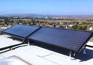 Solar panels on a rooftop, absorbing sunlight. Cityscape in the background, blue sky overhead.