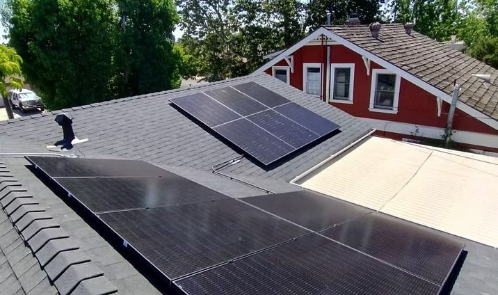 Solar panels on a dark shingled roof of a house with a red exterior.