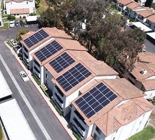 Solar panels on the rooftops of multi-unit apartment buildings with terracotta tile roofs.