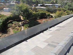 Solar panels installed on a roof, overlooking a yard with trees and a building.