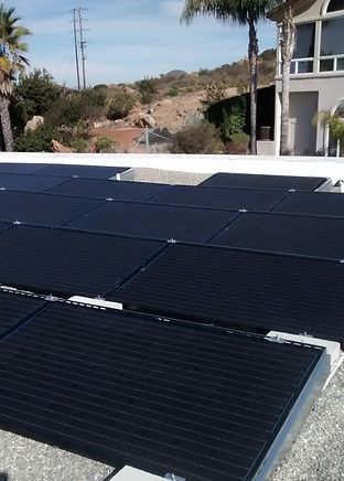 Solar panels on a flat roof, house in the background, sunny day.