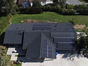 Overhead view of a dark-roofed house with solar panels installed on sections of the roof.