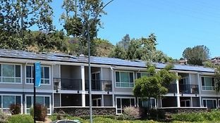 Row of townhomes with solar panels on the roof, nestled against a hillside with green trees.
