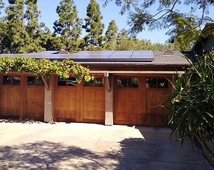 Wooden garage with solar panels on the roof, surrounded by trees and greenery.