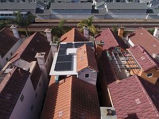 Aerial view of rooftops with solar panels; train tracks in background.