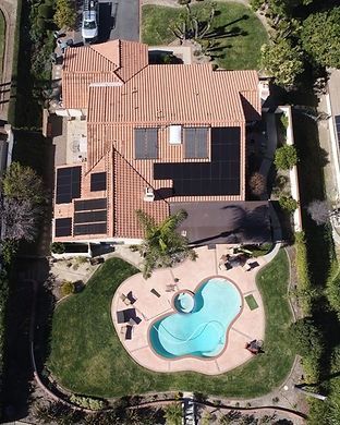 Aerial view of a house with solar panels on a terracotta roof, a swimming pool, and green lawn.