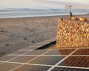 Solar panels on a building near a beach, with a stone chimney.