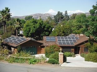 House with solar panels on the roof, surrounded by trees and a driveway.